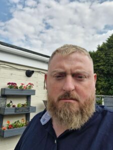 A photo of Andy from our parent's panel. He is outside with a blue and cloudy sky above him.