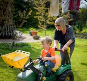 Older woman pushing a child on a digger in the garden.