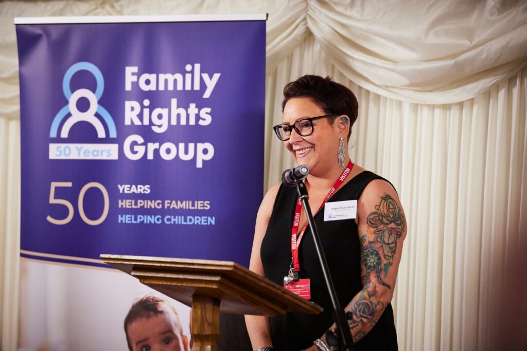 Angela Frazer-Wicks MBE smiling at the podium in front of a Family Rights Group 50 years banner