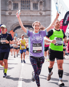 Photo of our runner crossing the finishing line of the London Marathon, arms in the air, smiling.
